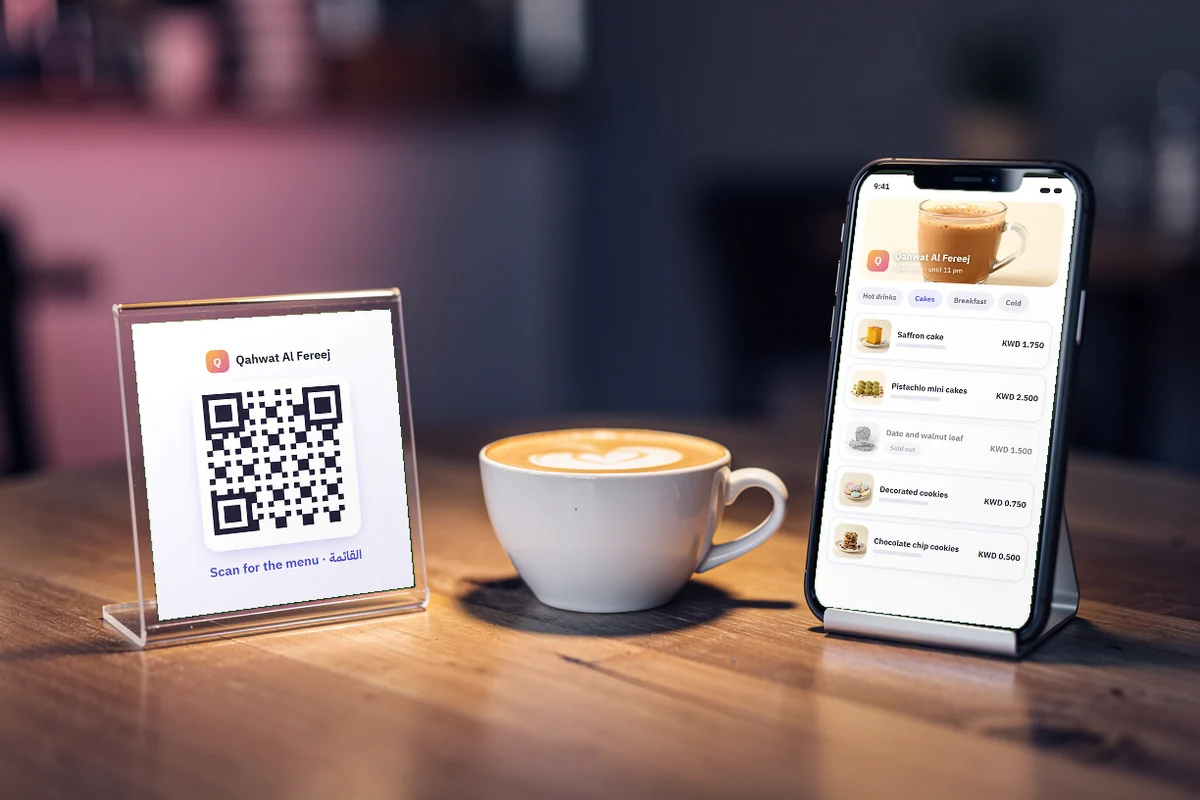 A guest holds a phone towards a small table stand beside a cappuccino in a warm café.